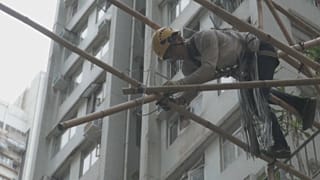 A worker builds bamboo scaffolding for an overhanging shop sign