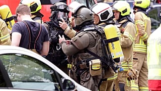 Police officers wearing gas masks and firefighters stand in front of a residential building in Ratingen, Germany, Thursday May 11, 2023. 