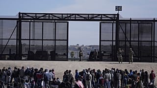 Migrants who crossed the border from Mexico into the U.S. wait next to the U.S. border wall. Seen from Ciudad Juarez, Mexico, March 30, 2023