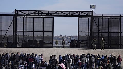 Migrants who crossed the border from Mexico into the U.S. wait next to the U.S. border wall. Seen from Ciudad Juarez, Mexico, March 30, 2023