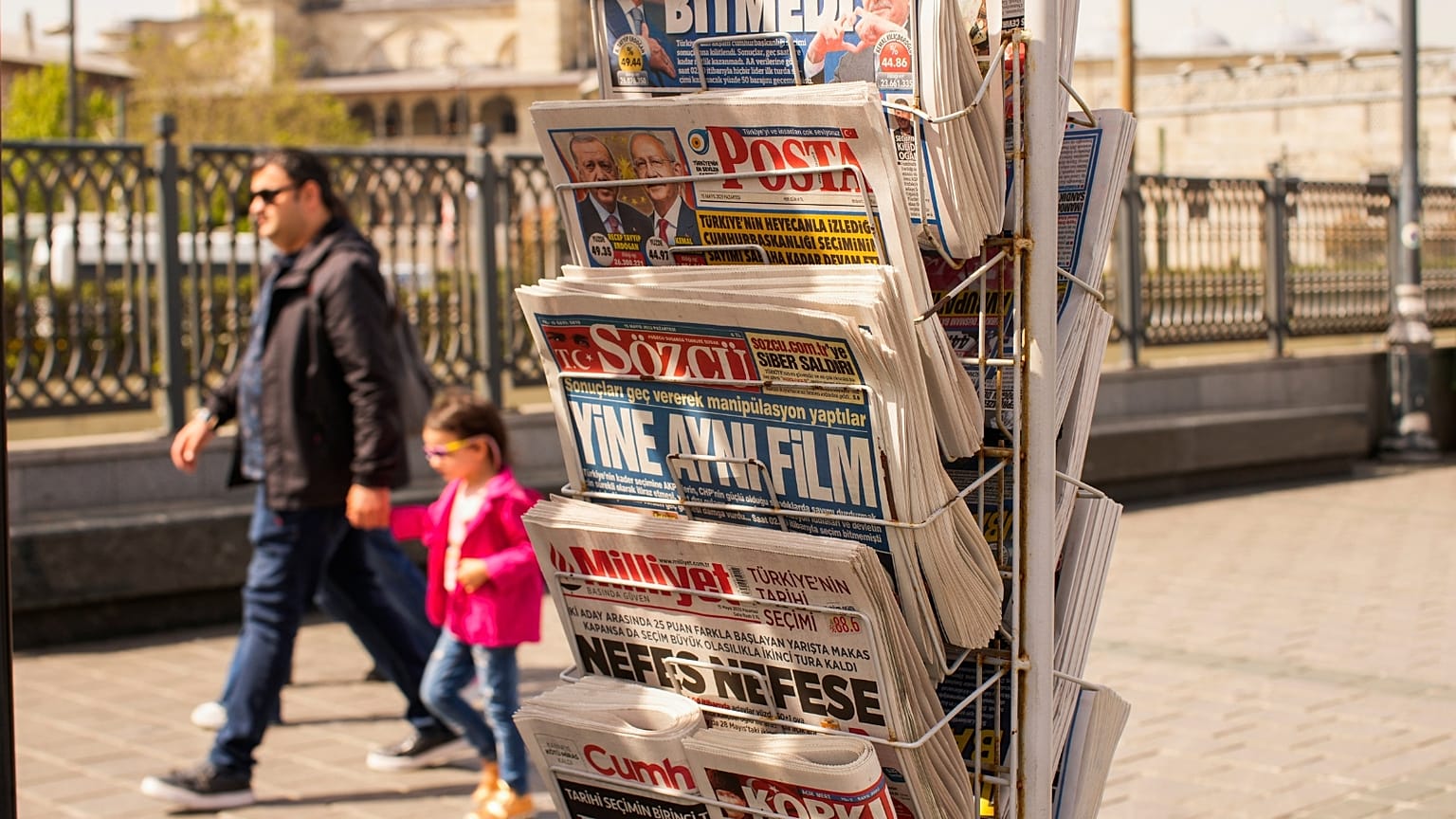 People walk past a rack with Turkish newspapers a day after the presidential election day, in Istanbul, Turkey, Monday, May 15, 2023.