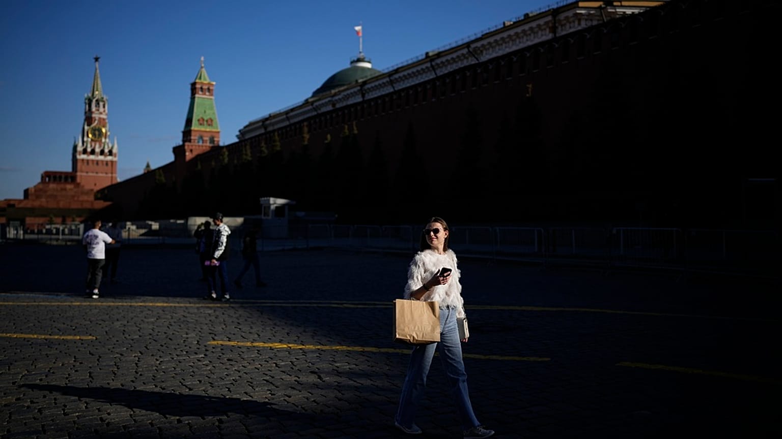 A woman walks in Red Square enjoying warm weather during sunset with the Kremlin Wall in background in Moscow, Russia, May 16, 2023