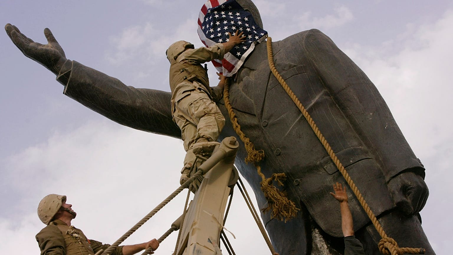 ABD'li asker, 9 Nisan 2003'te Irak'ın başkenti Bağdat'ta Saddam Hüseyin'in heykelini devirmeden önce heykelin yüzünü Amerikan bayrağıyla kapatıyor.