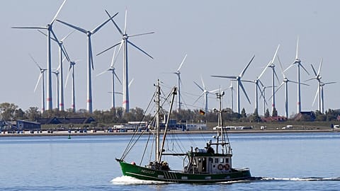 A fishing boat passes wind turbines between the island Langeoog and Bensersiel off the North Sea coast in Germany