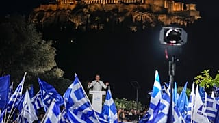 Supporters wave Greek flags as Greece's Prime Minister and New Democracy leader Kyriakos Mitsotakis gestures during his main election campaign rally in Athens.