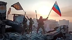 Yevgeny Prigozhin's Wagner Group military company members wave a Russian national and Wagner flag atop a damaged building in Bakhmut, Ukraine.