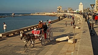 أشخاص يركبون عربة تجرها الخيول على طول كورنيش الواجهة البحرية في بنغازي شرق ليبيا، 26 مارس 2023 .
