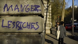 A man walks by a graffiti reading "eat the rich" in Paris.