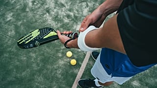 Person holding black and green padel racket