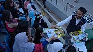 رجل يوزع ملصقات لولي العهد الأردني الأمير الحسين وخطيبته المهندسة رجوة السيف خلال حفل موسيقي في استاد رياضي في عمان.