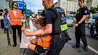 A police officer removes a demonstrator during a march by climate activists of the Last Generation group as they walk down Karl-Marx-Allee boulevard in Berlin.