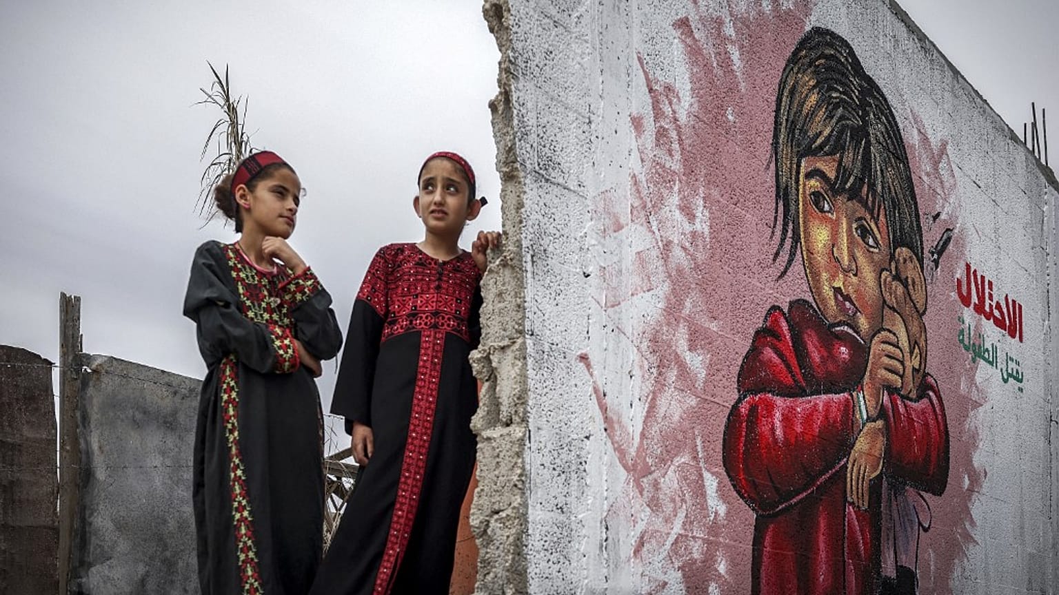 Zwei Mädchen kämmen sich die Haare vor einem Wandbild, die Teil einer Ausstellung im Gazastreifen ist