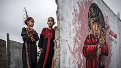 Zwei Mädchen kämmen sich die Haare vor einem Wandbild, die Teil einer Ausstellung im Gazastreifen ist