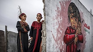 Zwei Mädchen kämmen sich die Haare vor einem Wandbild, die Teil einer Ausstellung im Gazastreifen ist