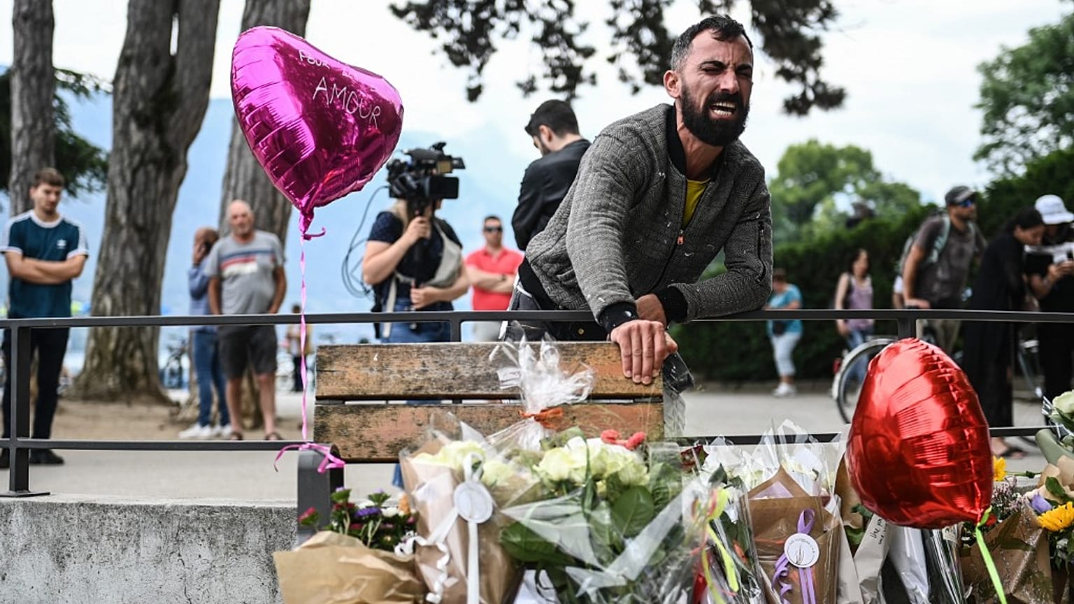 A man reacts in front of flowers and candles for the victims of a stabbing attack that occured the day before in the 'Jardins de l'Europe' parc in Annecy, France.