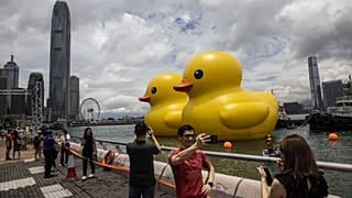 People take photos of two large inflatable yellow ducks called "Double Duck" by Dutch artist Florentijn Hofman in Victoria Harbour in Hong Kong on June 9, 2023.