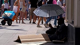 A man sits under an umbrella to shelter himself from the sun while begging for money in the street during hot weather in Madrid, Spain, Saturday, July 16, 2022.