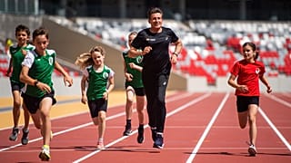 A WA elnöke, Sebastian Coe (középen) gyerekekkel fut a budapesti atlétikai világbajnokság futópályáján a Nemzeti Atlétikai Központban 2023.06.15-én.