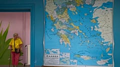 Idős nő áll Görögország térképe mellett egy szavazóhelyiségben Athénban 2023. június 25-én
