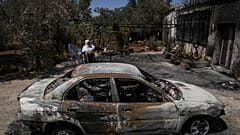 سيدة فلسطينية محجبة تقف بجوار سيارة تعرضت للحرق في ترمسعيا 