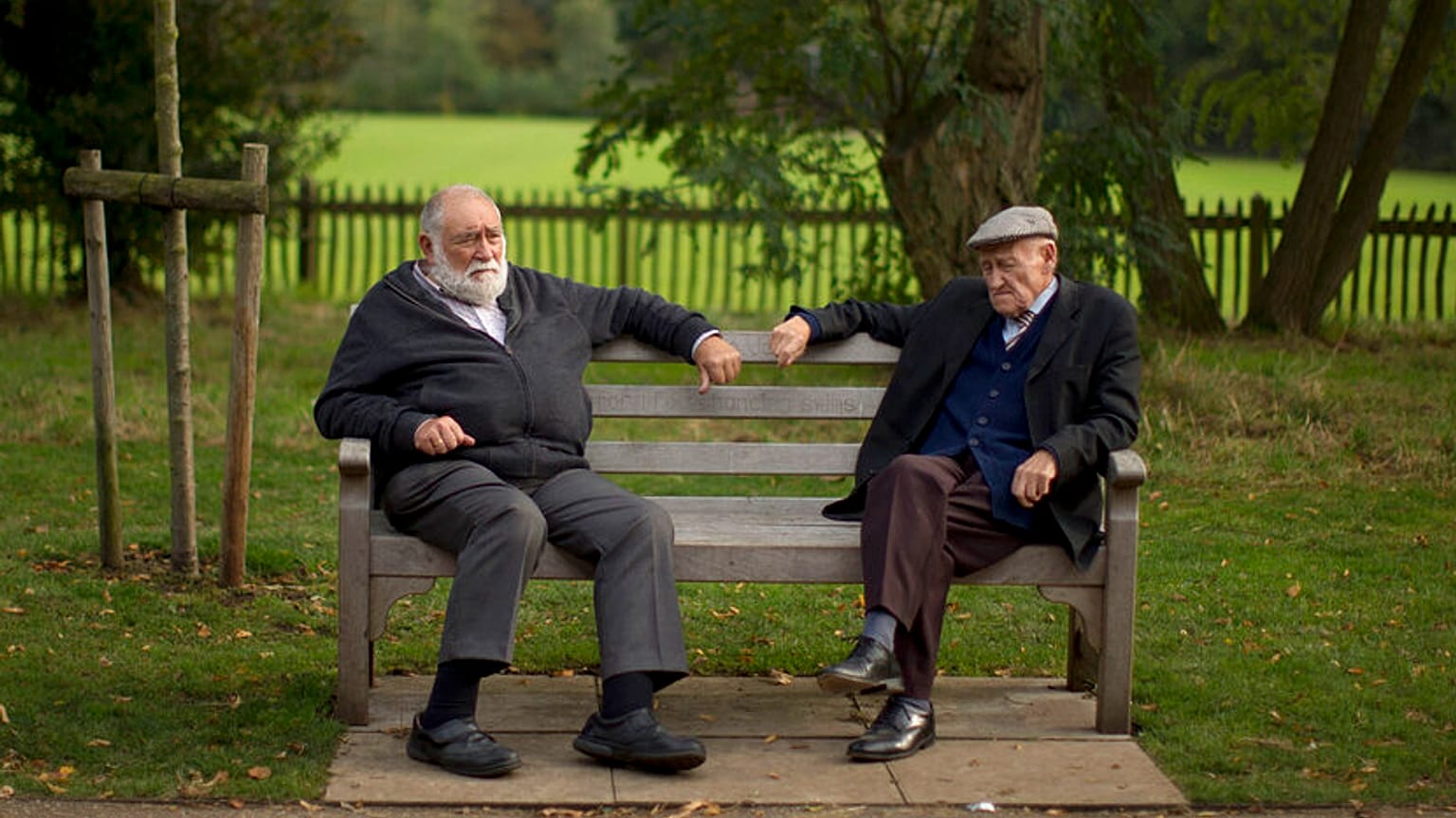 Two men sit on a bench on the periphery of the Hampstead Heath Heritage Festival, which is a celebration of old England on Hampstead Heath in London, Sunday, Oct. 7, 2012.