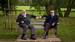 Two men sit on a bench on the periphery of the Hampstead Heath Heritage Festival, which is a celebration of old England on Hampstead Heath in London, Sunday, Oct. 7, 2012.