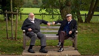 Two men sit on a bench on the periphery of the Hampstead Heath Heritage Festival, which is a celebration of old England on Hampstead Heath in London, Sunday, Oct. 7, 2012.