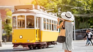 A tourist takes a photo of a tram in Lisbon