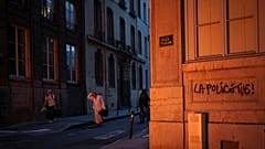 People pass by a wall illuminated by a burning barricade on which is written 'Police kills' in the center of Lyon, central France, Friday, June 30, 2023. 