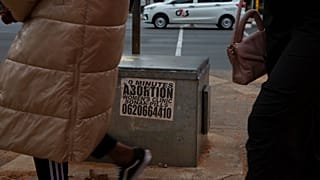 Kadınlar Haziran 2023'te Johannesburg, Güney Afrika'da kürtaj haplarının reklamını yapan bir etiketin önünden geçiyor.