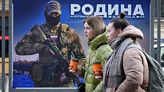 Niñas pasan frente a un puesto con la imagen de un militar ruso y las palabras "La patria que defendemos" en una exposición de fotografías militares en San Petersburgo.