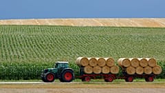 Ein Traktor mit Anhaengern transportiert Strohballen von einem Feld bei Dachau in Bayern. 