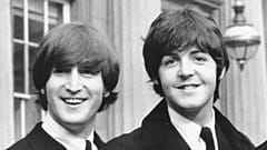 John Lennon, left, and Paul McCartney as they smile during a ceremony at Buckingham Palace in London, 1965
