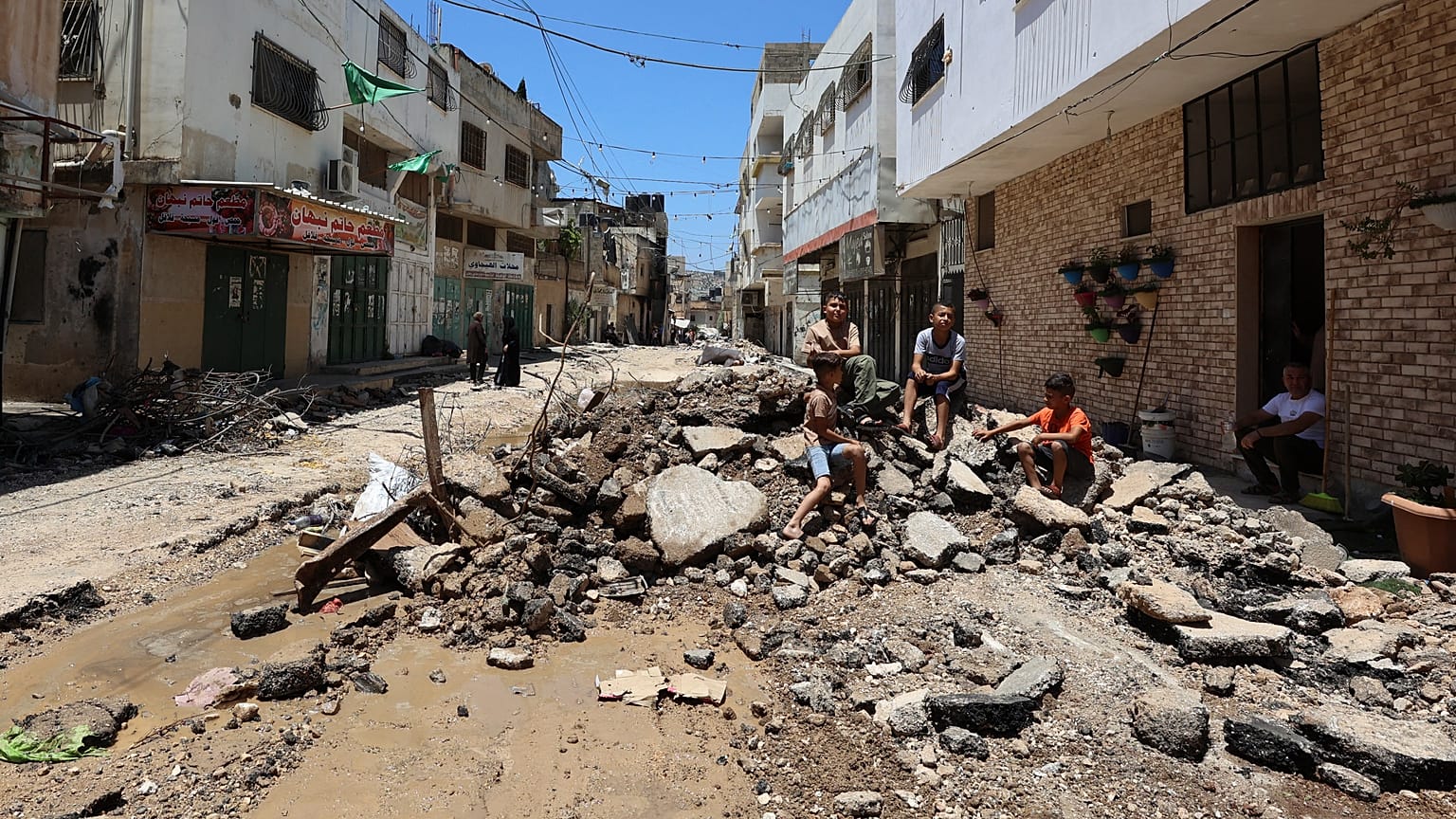 فلسطينيون يجلسون وسط الأنقاض على طول شارع في مخيم جنين للاجئين بالضفة الغربية المحتلة. 2023/07/06