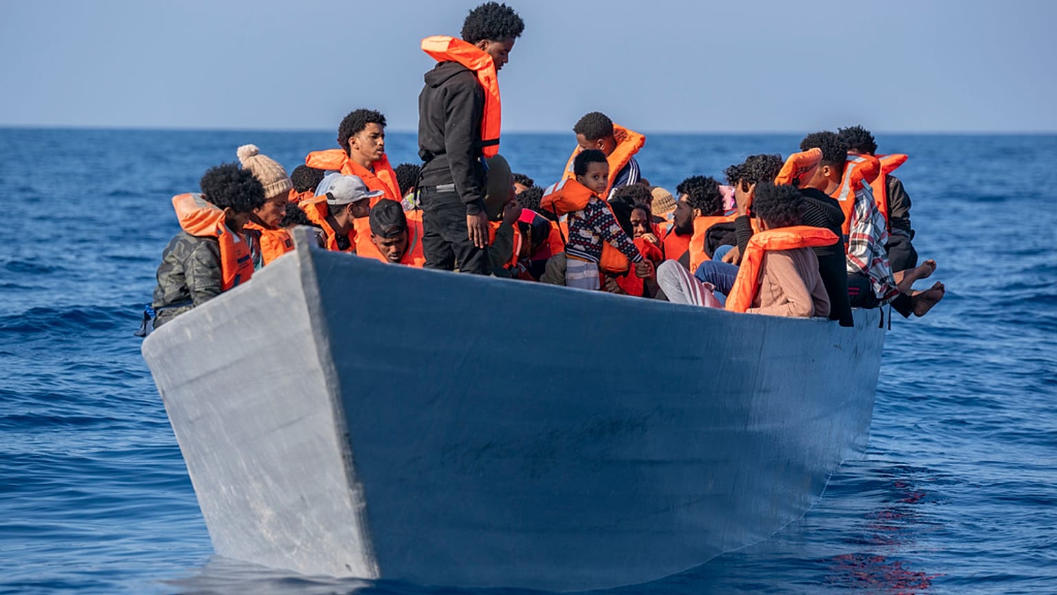  مهاجرون على ظهر قارب خشبي أثناء انتظارهم لتلقي المساعدة من قبل عمال الإغاثة من منظمة "أوبن آرمز"، في البحر الأبيض المتوسط، 17 يونيو 2023