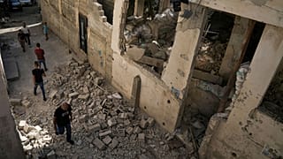 فلسطینی‌ها از کنار خانه‌ای آسیب دیده در اردوگاه آوارگان جنین در کرانه باختری عبور می‌کنند، پنجم ژوئیه ۲۰۲۳