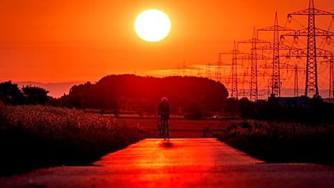 A man rides his bike on a small road in the outskirts of Frankfurt, Germany, as the sun rises on July 9, 2023. 