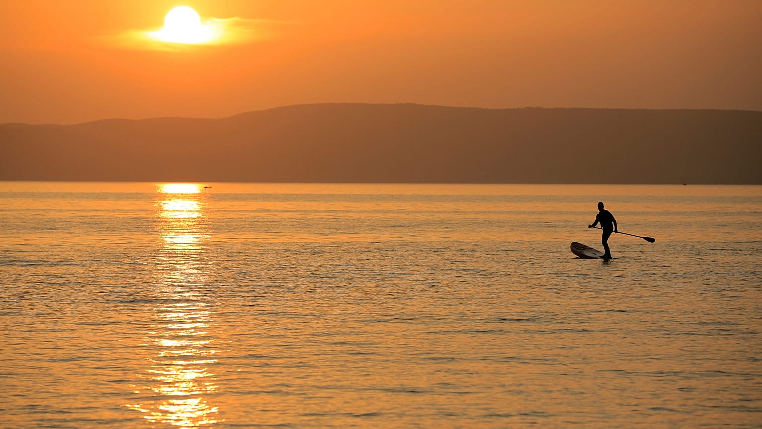 A man steers his SUP board during sunset at the Lake Balaton in Fonyod, Hungary, Tuesday, July 27, 2021