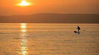 A man steers his SUP board during sunset at the Lake Balaton in Fonyod, Hungary, Tuesday, July 27, 2021