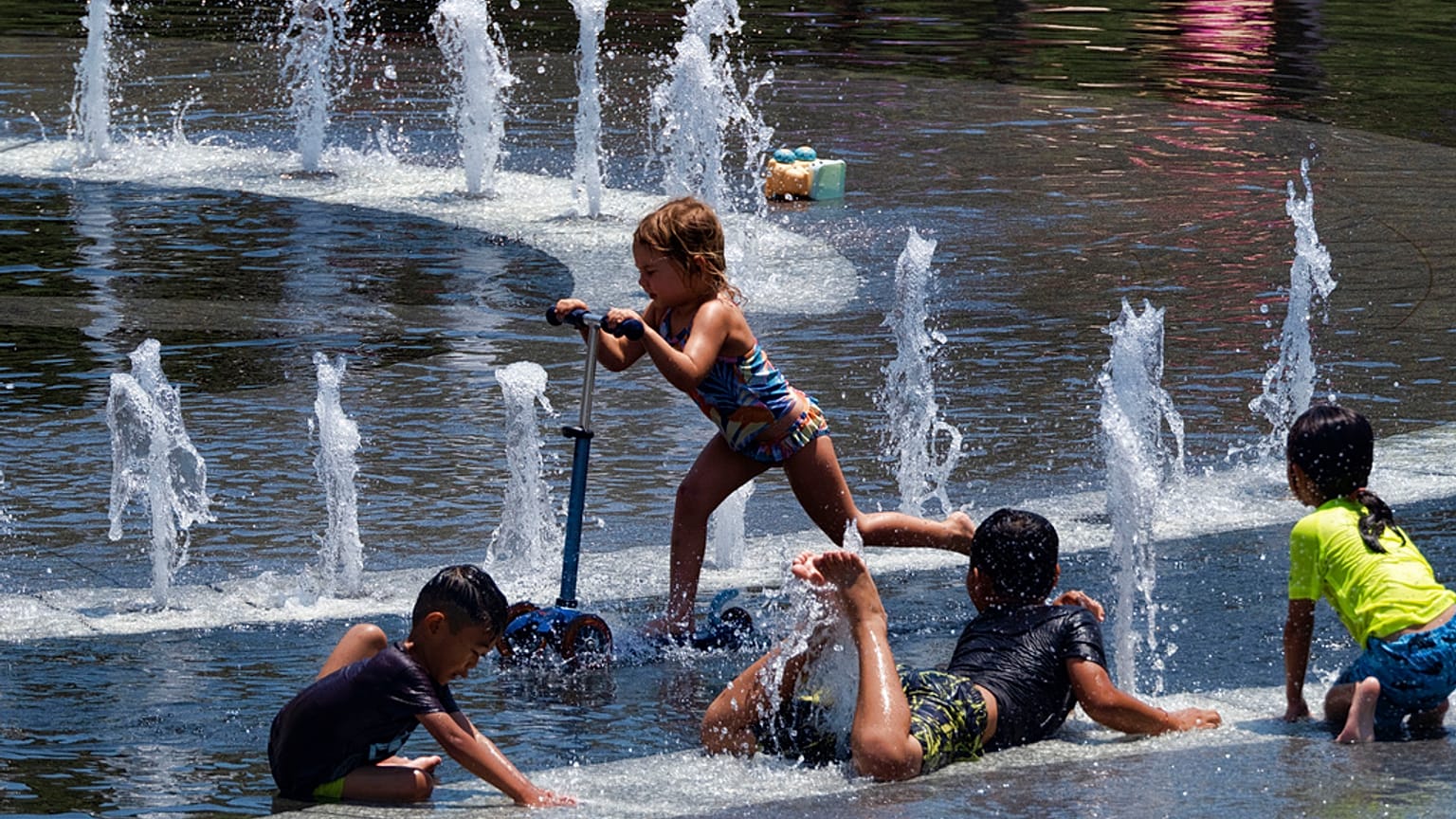 Niños de la ciudad intentan refrescarse en una fuente de agua en Grand Park, en el centro de Los Ángeles, el domingo 16 de julio de 2023.
