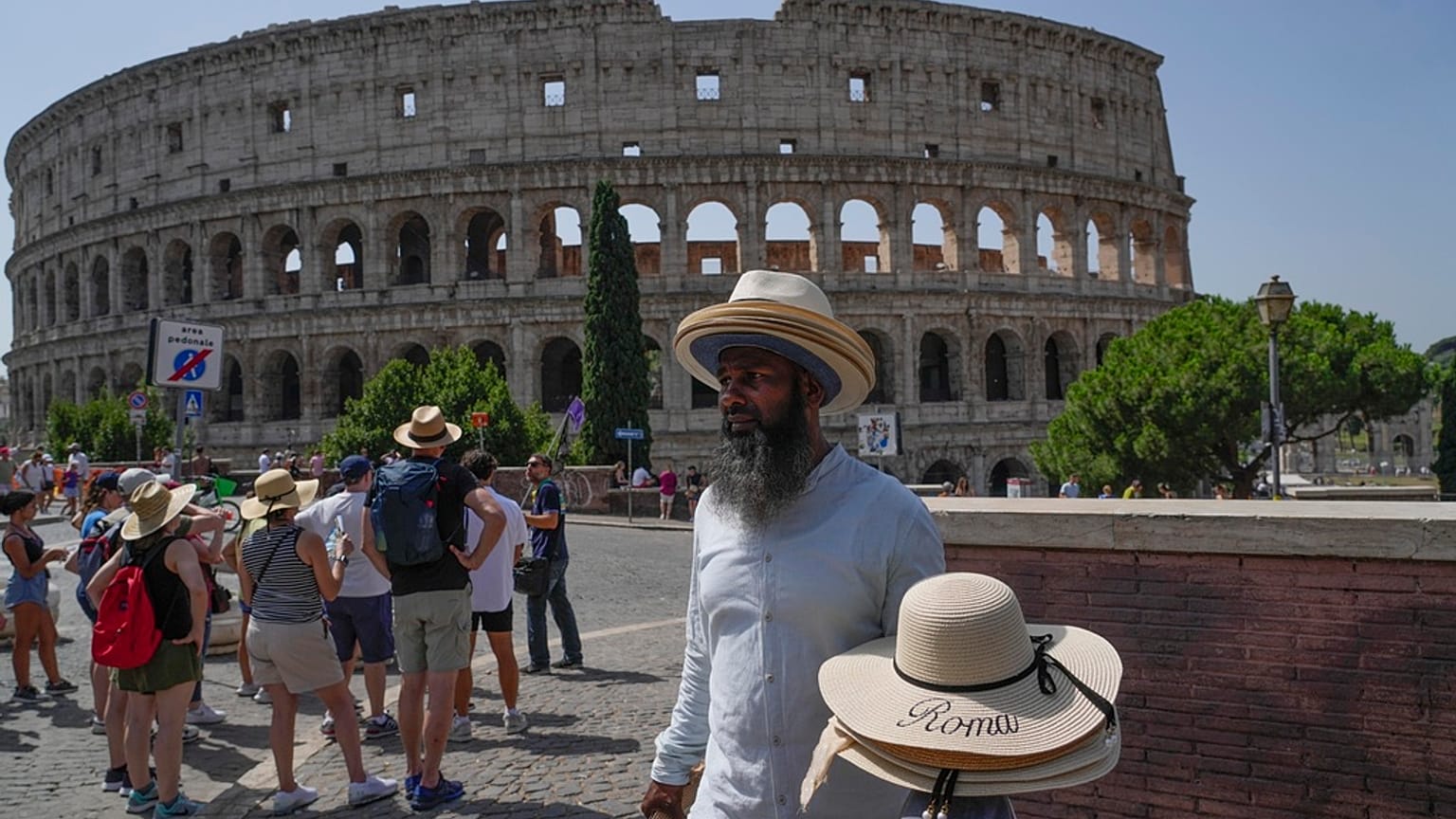 A street vendor walks with hats in front of the Colosseum in Rome