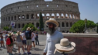 A street vendor walks with hats in front of the Colosseum in Rome