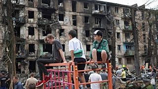 Ukrán gyerekek egy lebombázott panelház előtti játszótéren