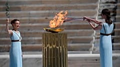 Die griechische Schauspielerin Xanthi Georgiou entzündet als antike griechische Hohepriesterin die olympische Fackel, während die Choreografin Artemis Ignatiou bei der Übergabe der olympischen Flamme zusieht.