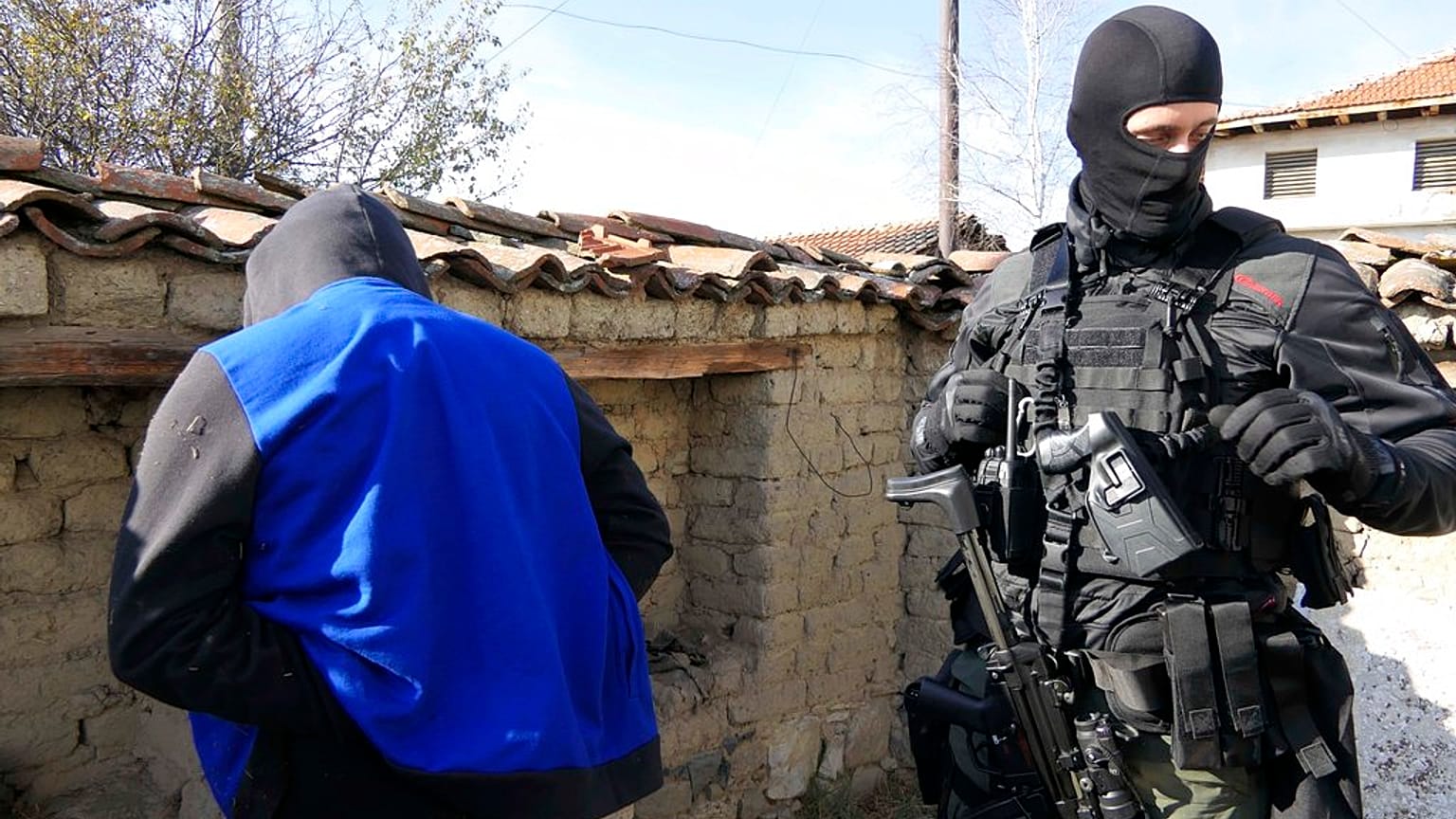 FILE - a police officer guards a detained person during a police raid in Sofia, Bulgaria in 2018.