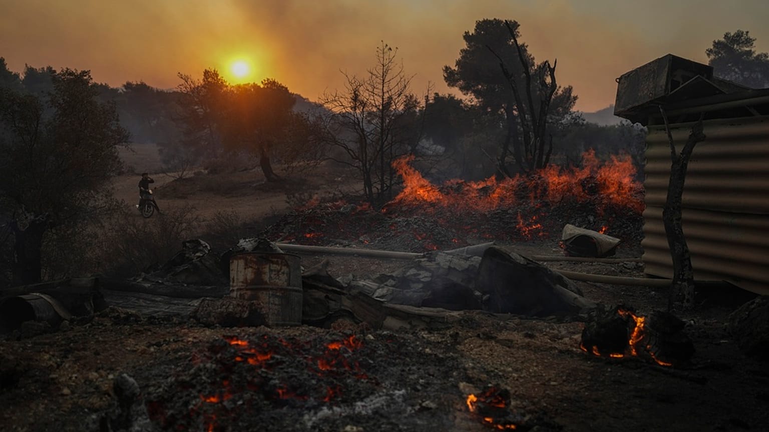 A man on a motorcycle looks at a shipyard which is on fire in Mandra west of Athens