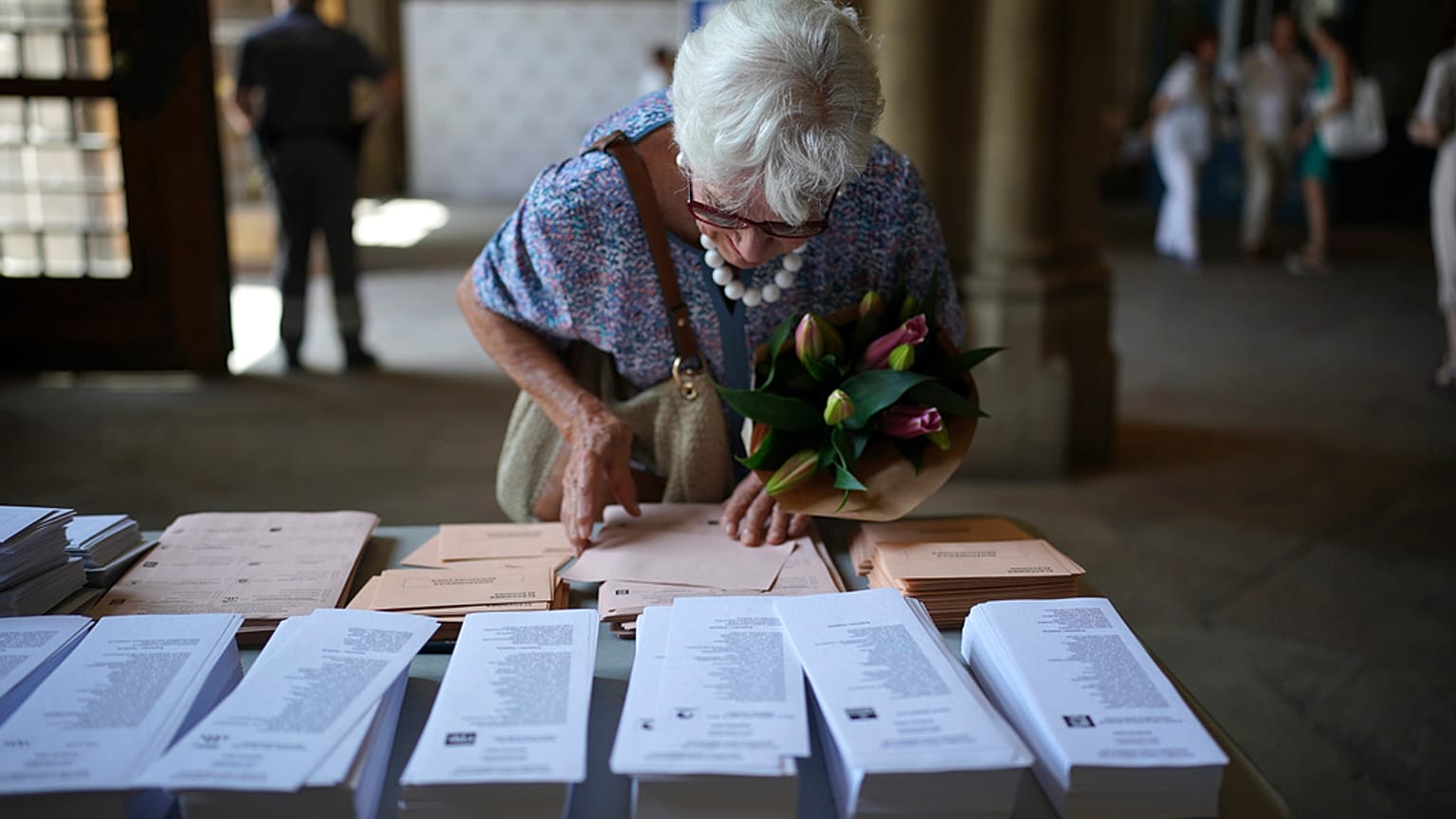 A woman holding a bouquet of flowers tries to select her ballots to vote at a polling station in Barcelona, Spain, Sunday July 23, 2023. 