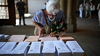 A woman holding a bouquet of flowers tries to select her ballots to vote at a polling station in Barcelona, Spain, Sunday July 23, 2023. 