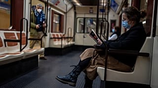 Eine Frau mit einer Gesichtsmaske liest ein Buch in einer U-Bahn in Madrid.
