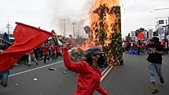 Protesters run past a giant military boot after setting it up on fire as they march towards Congress for a demonstration in Quezon City, suburban Manila on July 24, 2023